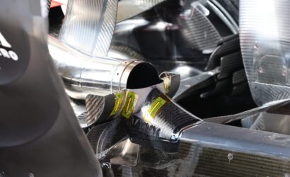 Close-up of shiny metallic ducting and carbon-fiber panels with yellow calibration labels, inside a vehicle or aircraft structure.