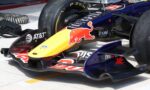 Close-up of a Red Bull Formula 1 car nose in the pit area, showing sponsor decals and the front wing authority plate area on a yellow-to-red livery.
