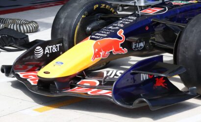 Close-up of a Red Bull Formula 1 car nose in the pit area, showing sponsor decals and the front wing authority plate area on a yellow-to-red livery.