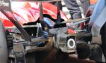 Close-up of a high-performance open-wheel race car rear, featuring carbon fiber chassis, exhaust pipe, and diffuser components.