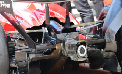 Close-up of a high-performance open-wheel race car rear, featuring carbon fiber chassis, exhaust pipe, and diffuser components.