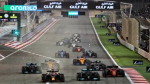 Nighttime Formula 1 race start with several cars lined up on the grid and the track lit up with sponsor banners along the pit straight.