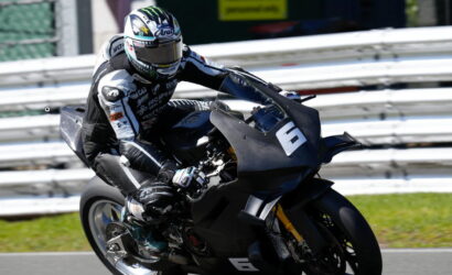 Motorcycle racer in black gear leaning into a turn on a race track.