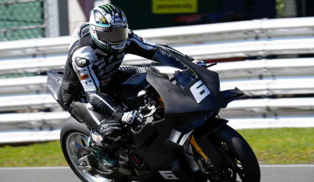 Motorcycle racer in black gear leaning into a turn on a race track.