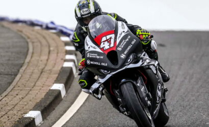 Motorcycle racer leaning into a sharp turn on a race track, wearing a black suit and helmet with the number 47 on the bike.