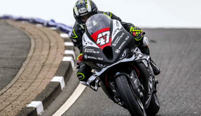 Motorcycle racer leaning into a sharp turn on a race track, wearing a black suit and helmet with the number 47 on the bike.