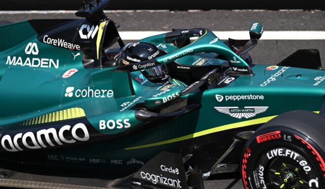Close-up of a teal Formula E race car cockpit with a driver in a helmet, showing sponsor logos like Coherent(codec?) Cognizant, BOSS, Valvoline, and Aston Martin on the car body and wheel.