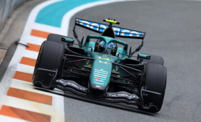 Formula 1 car in green livery rounds a corner on a racing track, sponsor logos visible on the nose and wings
