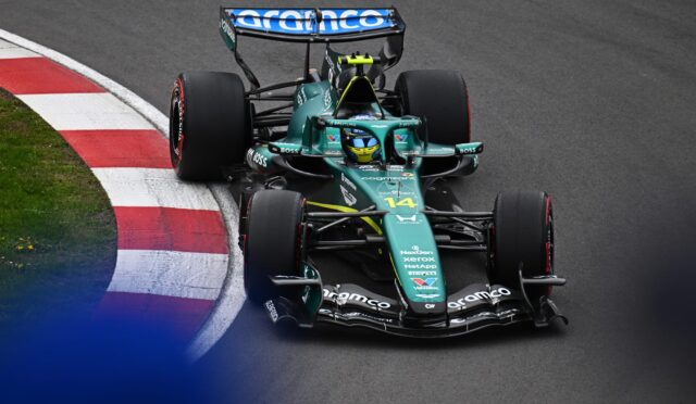 Green Formula 1 car seen from above turning into a curbed corner on a dark race track, sponsor logos visible on the nose and wings.