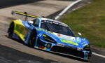 Blue and yellow race car taking a left-hand turn on a racetrack, sponsor decals visible on the bodywork and rear wing.