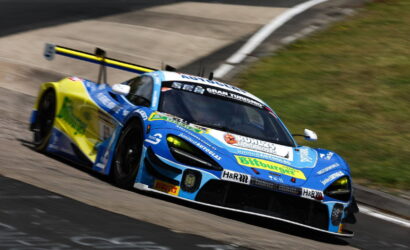 Blue and yellow race car taking a left-hand turn on a racetrack, sponsor decals visible on the bodywork and rear wing.