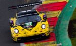 Yellow Porsche race car on a racetrack, riding the red-and-yellow curbing with Manthey branding on the rear wing and sponsors on the body.