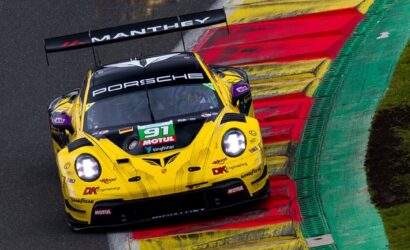Yellow Porsche race car on a racetrack, riding the red-and-yellow curbing with Manthey branding on the rear wing and sponsors on the body.
