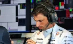 Professional race driver wearing a headset, studying notes in a control room with multiple monitor displays.