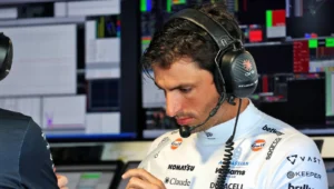 Professional race driver wearing a headset, studying notes in a control room with multiple monitor displays.