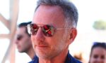 Middle-aged man wearing aviator sunglasses outdoors, close-up portrait with a reflective lens showing a red-clad figure in the reflection