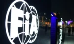 Illuminated FIFA logo with a globe and gear motif at night on an outdoor sign.