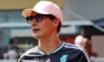 Man wearing a pink cap and sunglasses, in a dark sports jersey, looking to the left outdoors.