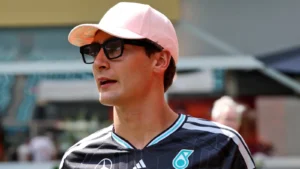 Man wearing a pink cap and sunglasses, in a dark sports jersey, looking to the left outdoors.