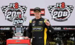 Race car driver in a SPARE Motorsports suit poses with the winner’s trophy at the FR8 Racing 208 event, Atlanta Motor Speedway backdrop.