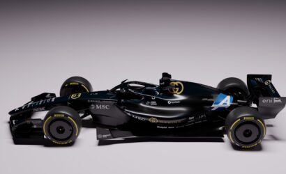 Black Formula 1 race car shown from the side with gold logos and sponsor decals on a light gradient background.