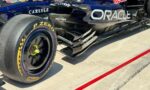Close-up of a Formula 1 car's rear-left tire and sidepod, showing blue/black livery, Oracle logo, and Pirelli tire markings on a sunny pit lane.