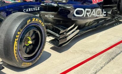 Close-up of a Formula 1 car's rear-left tire and sidepod, showing blue/black livery, Oracle logo, and Pirelli tire markings on a sunny pit lane.
