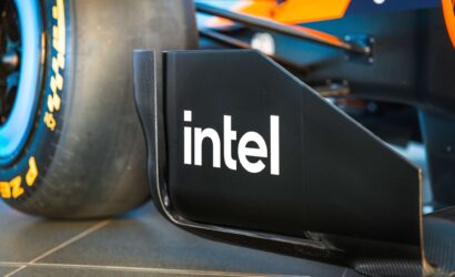 Close-up of a race car's sidepod featuring the Intel logo and bold blue‑orange bodywork, with a tire in the background, conveying branding on a Formula 1 car.