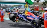 Red Bull Racing Formula 1 car with Oracle sponsor livery in the pit lane, crew members in orange safety vests standing nearby as a mechanic works on the vehicle.