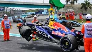 Red Bull Racing Formula 1 car with Oracle sponsor livery in the pit lane, crew members in orange safety vests standing nearby as a mechanic works on the vehicle.