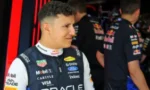 Racing driver in Oracle Red Bull Racing suit standing in a team garage, looking off to the side.