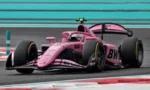 Pink Formula 1 race car speeding around a track with turquoise barriers in the background, conveying motion and competition.