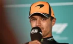 Male race car driver in an orange cap speaks into a microphone during a post-race interview.
