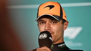 Male race car driver in an orange cap speaks into a microphone during a post-race interview.