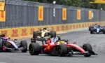 Red Formula 1 car leads a pack on a race track, with DHL banners along the barrier walls behind.