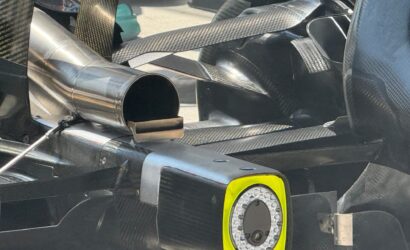 Close-up of a race car's carbon fiber body with a circular exhaust outlet and a yellow-framed wheel opening nearby.