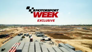 Motorsport Week Exclusive logo above a race track with cars and construction on a clear day.