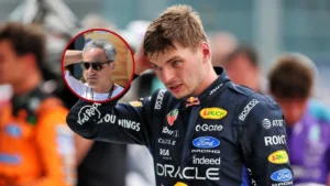 Motorsport driver in a suit with sponsor logos stands on track; a man wearing sunglasses is circled in red in the background.