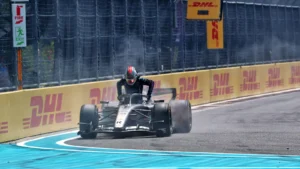 Open-wheel race car on a track taking a corner, driver wearing a helmet with DHL banners along yellow barriers in the background.