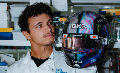 Man in a white lab coat standing next to a glossy, colorful racing helmet with Monster Energy logos.