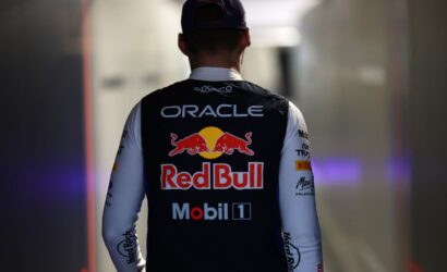 Back view of a person wearing a Black Oracle-Red Bull racing vest in a dim hallway, facing away from the camera, cap on.