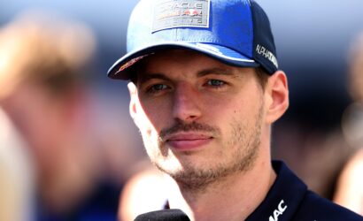 Close-up of a man in a blue cap with Oracle Red Bull Racing patch, speaking into a microphone during an interview.