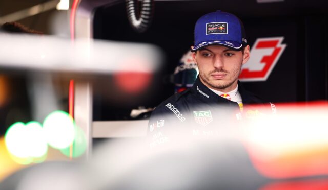 Portrait of a race car driver in a blue Oracle Red Bull cap, in a pit/garage setting with sponsor logos on the suit above.