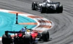 Red Formula 1 car leading through a sharp corner, with a silver race car close behind on a grey tarmac track, in a racing scene.