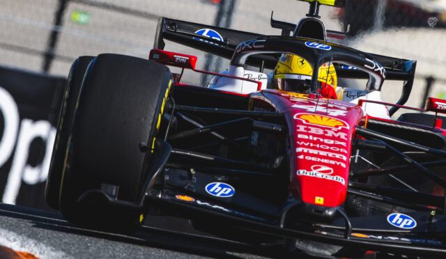 Red Formula 1 car with a yellow helmeted driver speeding along the track, close to the wall and barriers, sponsor logos visible.