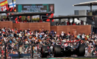 Formula 1 car racing past a crowded grandstand with flags and banners in the background (Mercedes AMG Petronas signage)