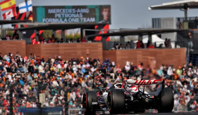 Formula 1 car racing past a crowded grandstand with flags and banners in the background (Mercedes AMG Petronas signage)