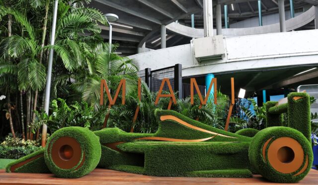 Outdoor urban garden installation with manicured green turf sculptures and large orange letters spelling MIAMI against a concrete overpass.