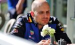 Male race car driver in a blue sponsor-laden suit, looking down while holding white flowers.