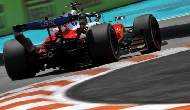 Rear three-quarter view of a red Formula 1 race car speeding along a track, with motion blur and orange-and-white curbs in the foreground.
